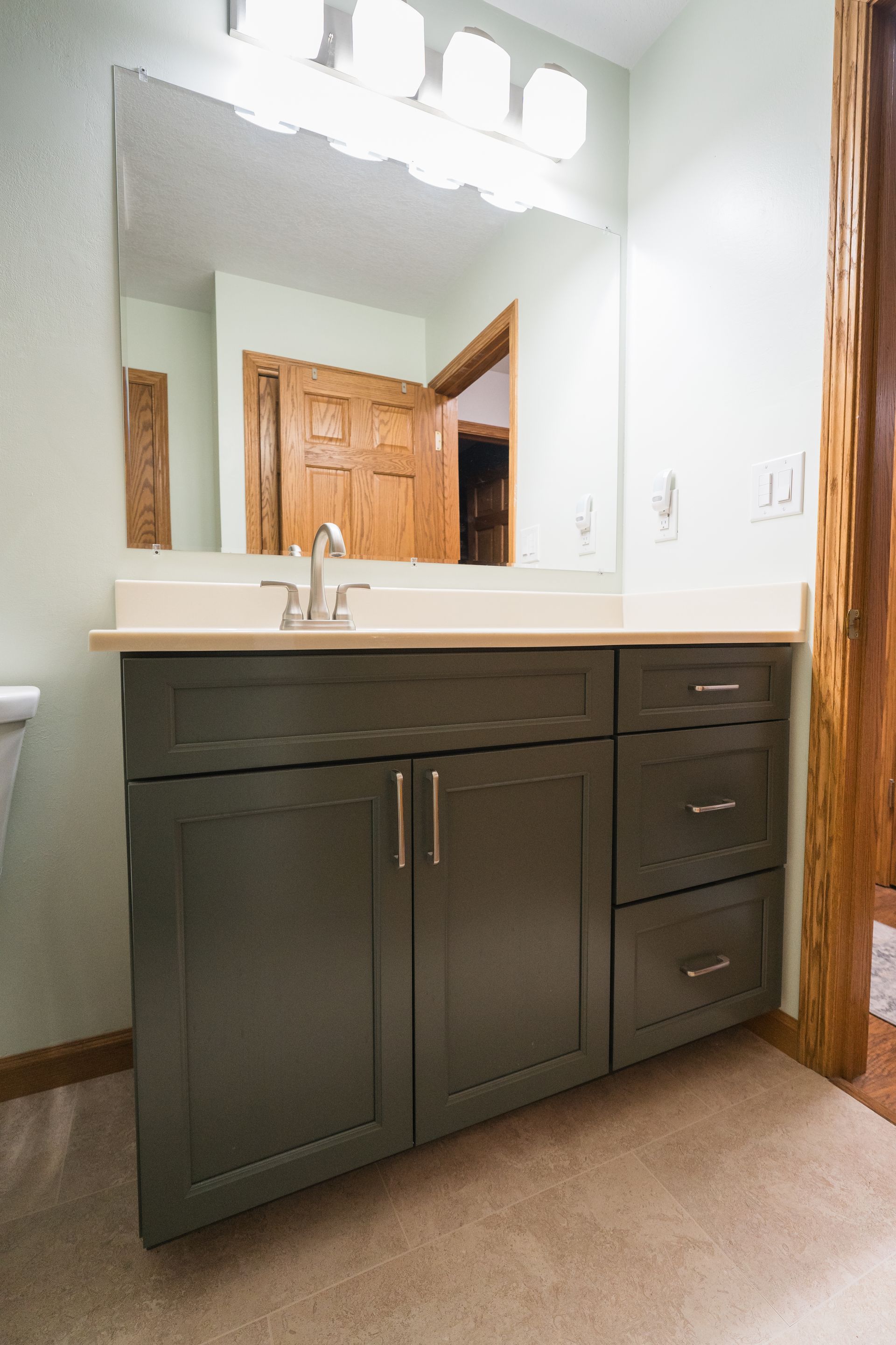 Bathroom vanity with dark wood cabinets, white countertop, mirror, and overhead lights