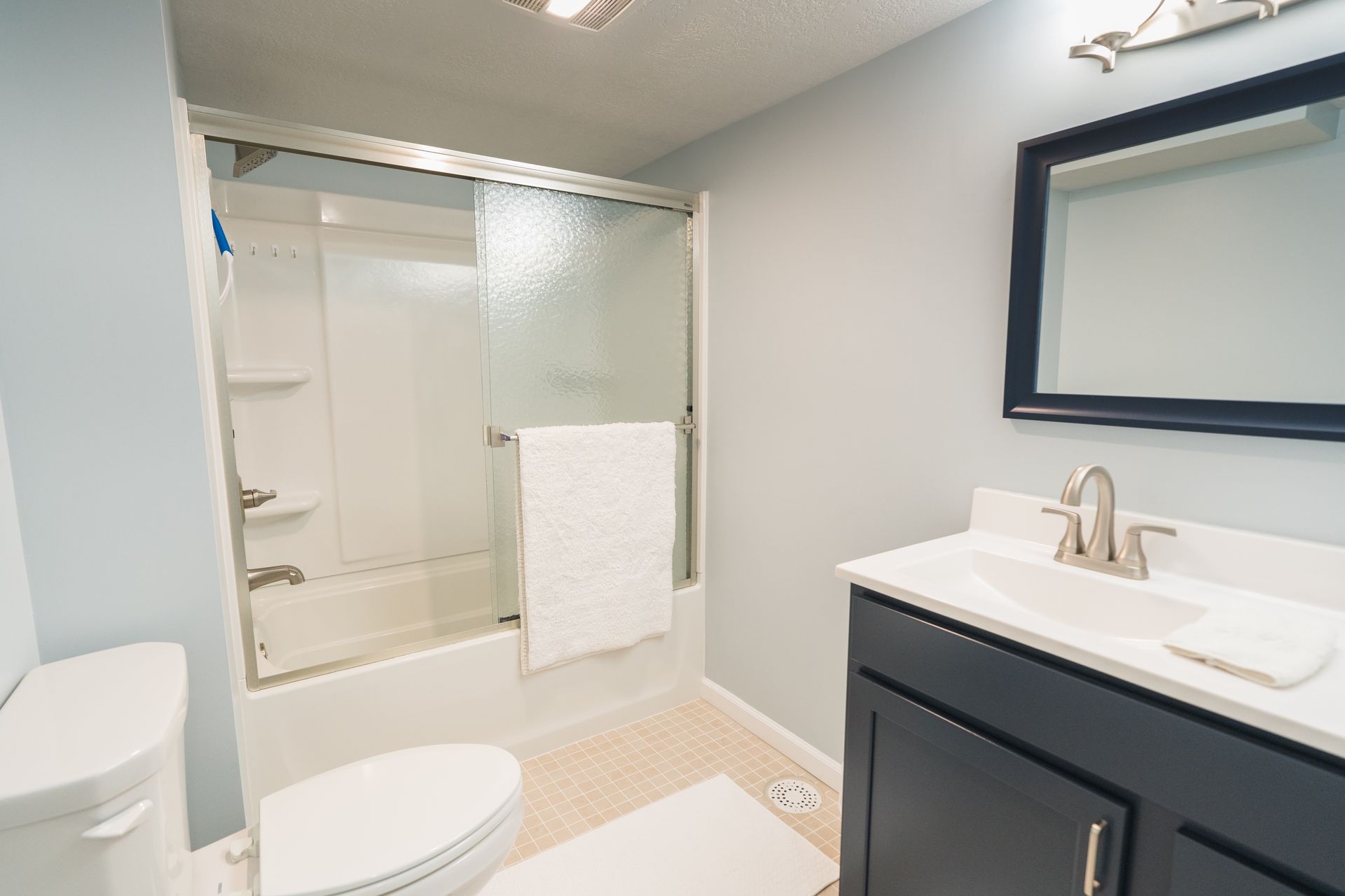 Modern bathroom with shower-tub combo, white vanity, and dark mirror frame