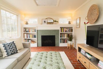 Bright living room with fireplace, bookshelves, sofa, TV, and brick floor