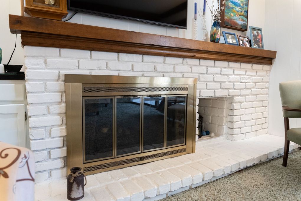White brick fireplace with brass screen and wooden mantel in a living room