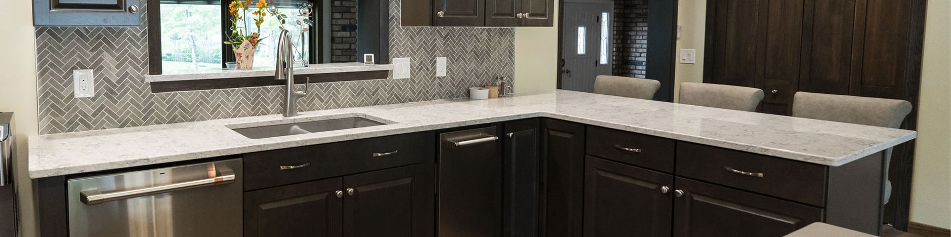 Modern kitchen with dark cabinets, light countertop, tile backsplash, window, and sink sink under the window