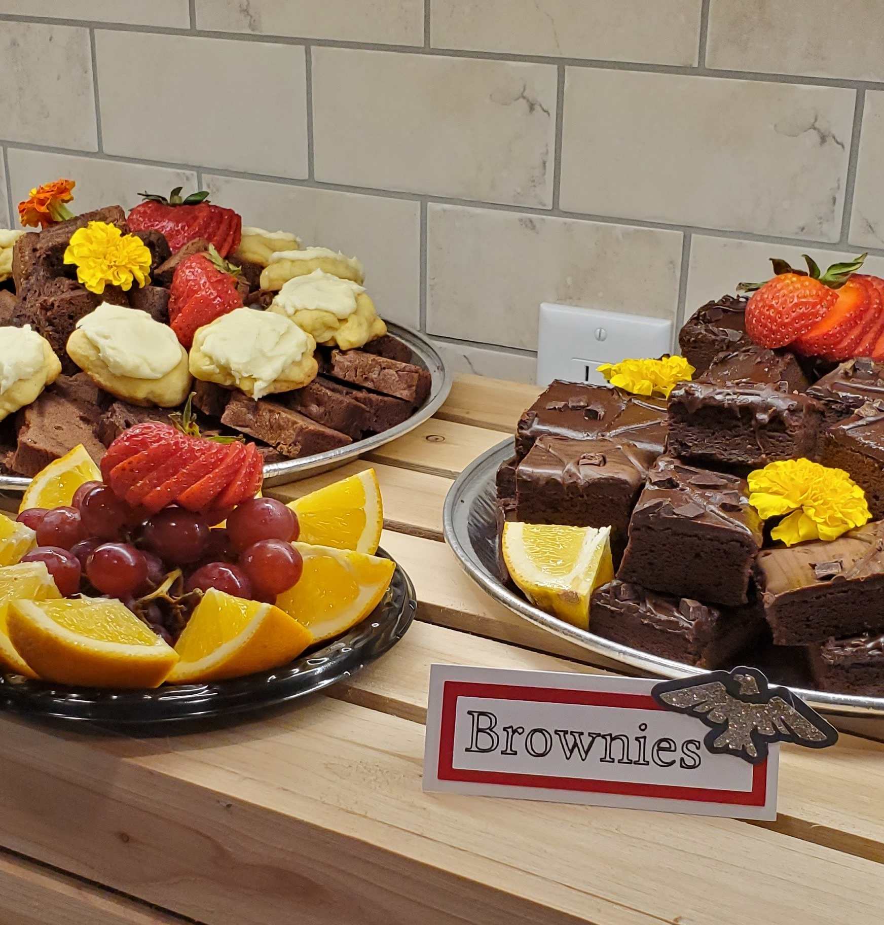 A tray of brownies sits next to a tray of fruit