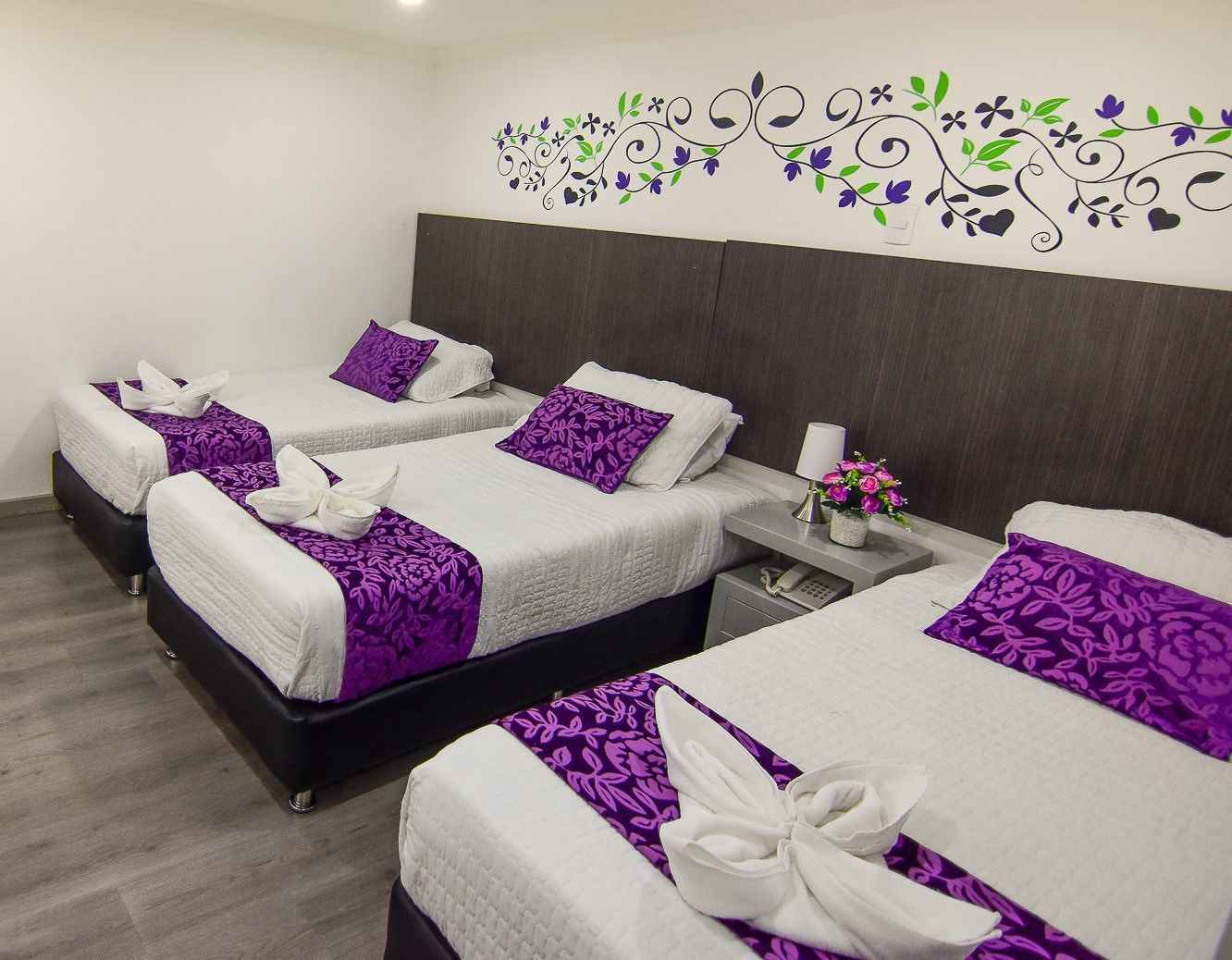 A hotel room with three beds and purple sheets