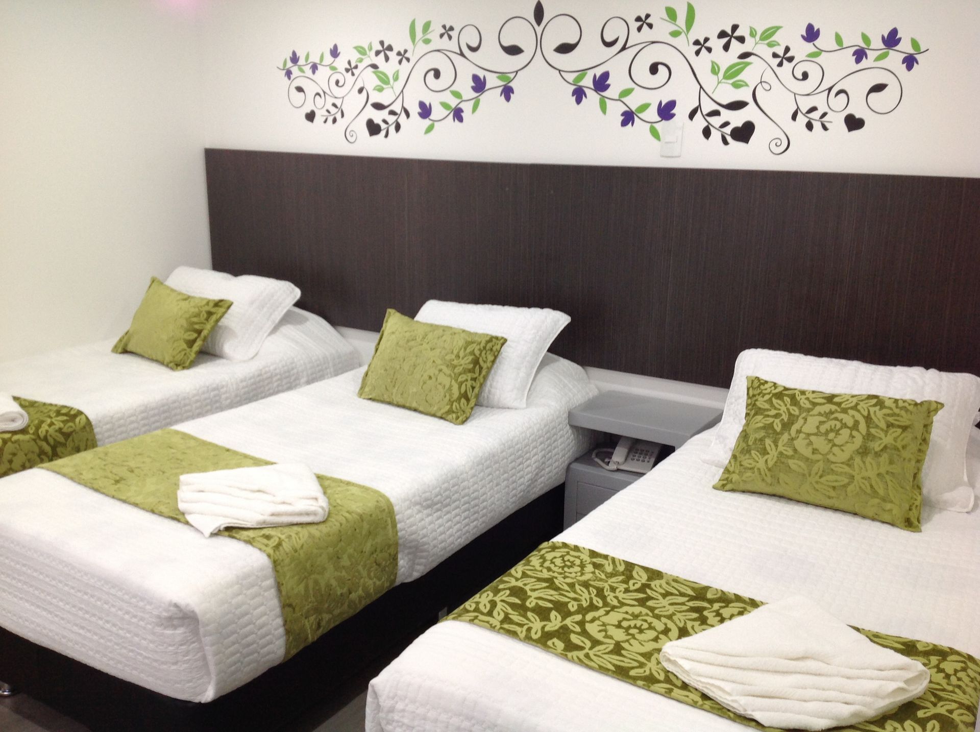 Three beds in a hotel room with green sheets and pillows