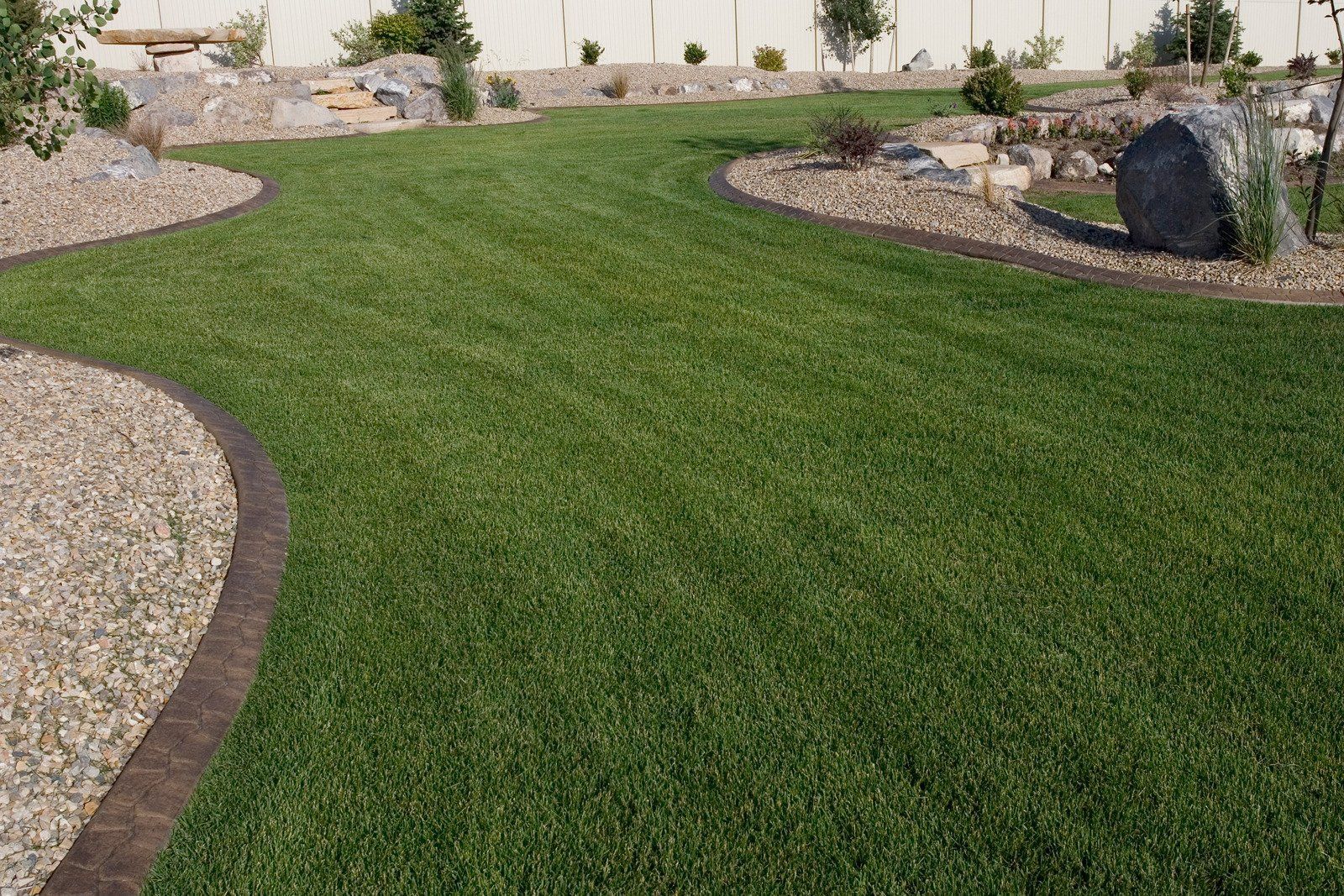 A lush green lawn is surrounded by gravel and rocks