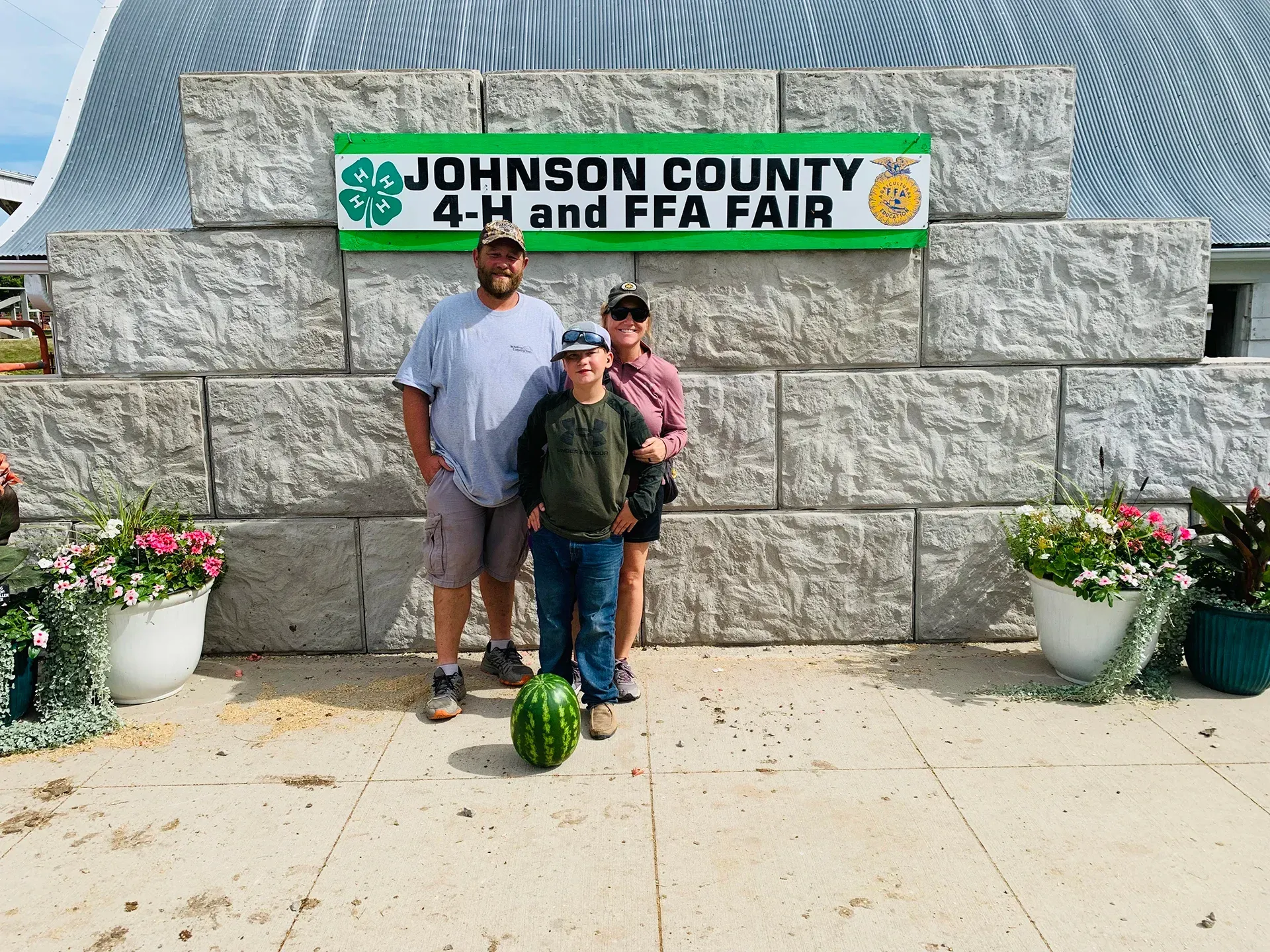Two boys posing in front of a Johnson County 4-H and FFA Fair sign with a watermelon on the ground.