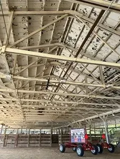 Old barn interior with exposed rafters and a red tractor parked inside.