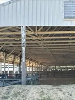 Open-sided livestock barn with metal roof and pens, with a pile of feed or bedding in the foreground
