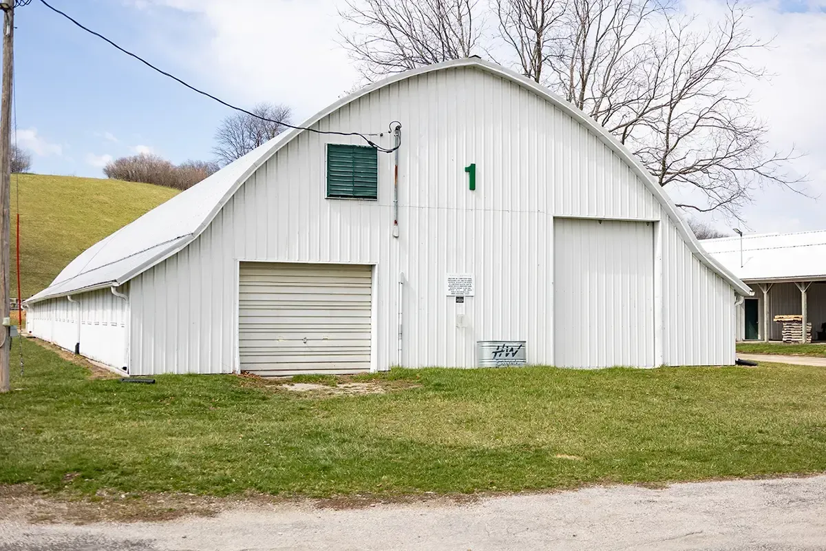 White barn with a garage door and green number 1, beside a gravel road and grass.