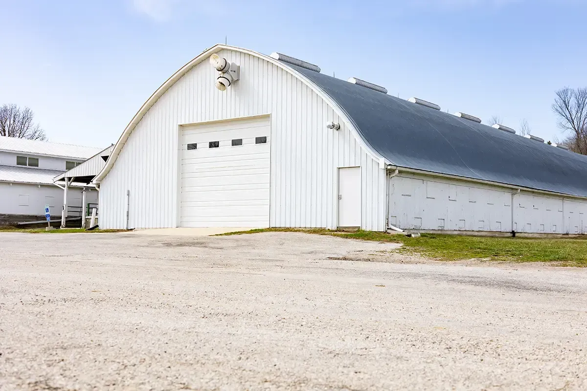 White metal barn-style building with a large garage door on a gravel lot under a clear sky