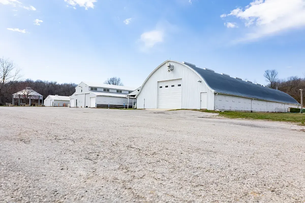 White barn and farm buildings on a gravel lot under a blue sky