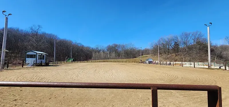Open field with wooden fence, leafless trees, and a blue sky at a park.