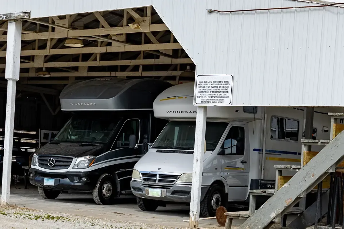 Two white vans and a black SUV parked in a covered garage with a wooden staircase