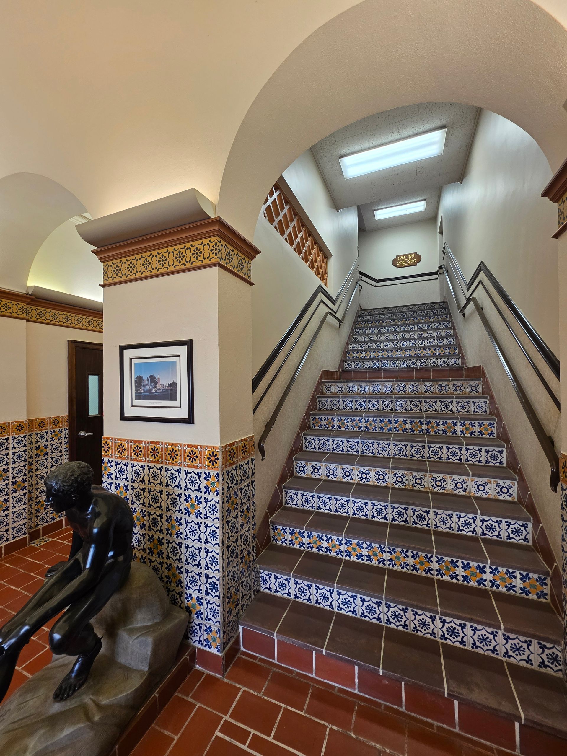 Staircase with tile risers, archways, and a statue, in a building with a Southwestern design.