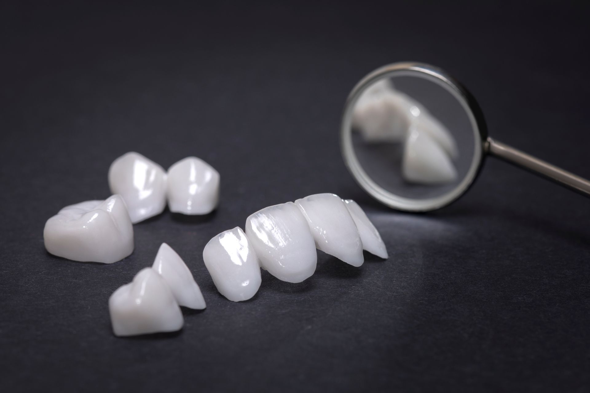 Dental veneers on dark surface, with dental mirror reflecting them.