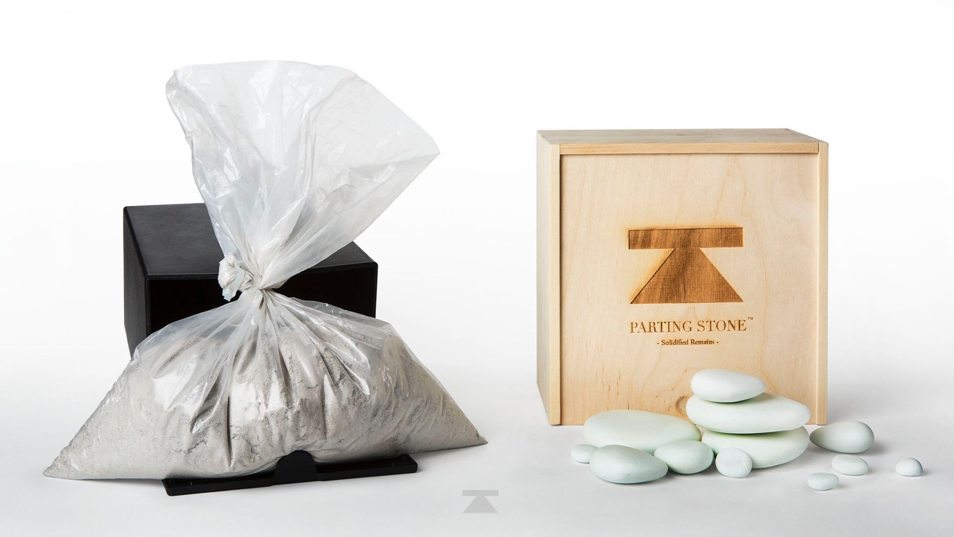 Silver gift bag with black base beside a wooden box of oval green-and-white soaps on a white background
