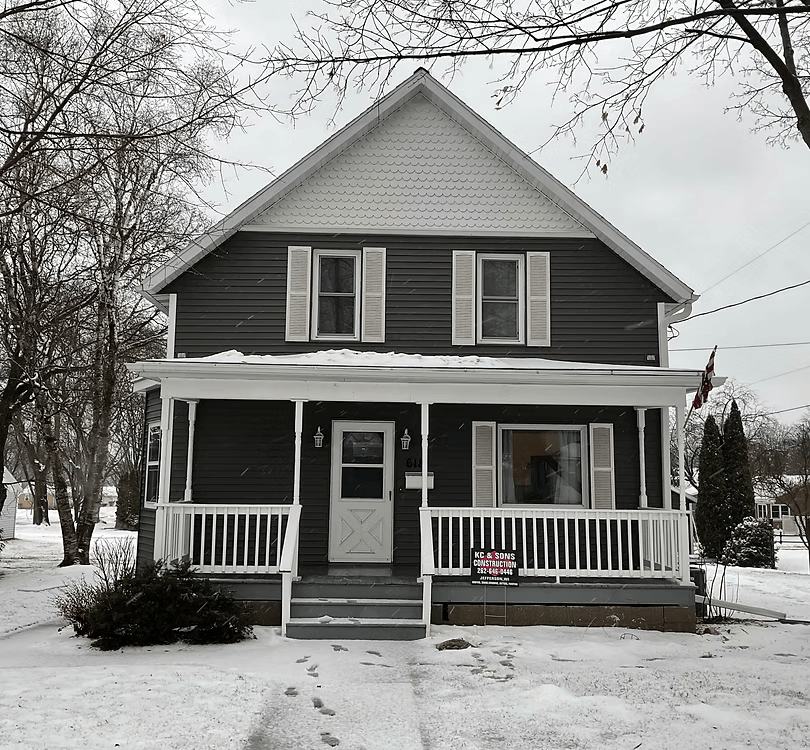 Snow-covered gray house with a front porch and white trim on a winter day
