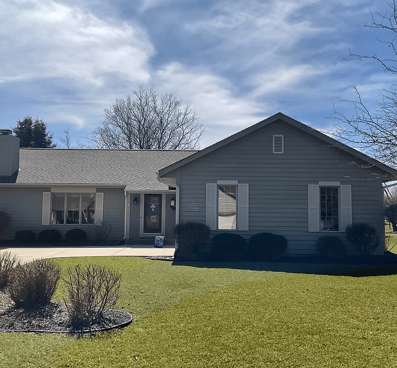 Single-story gray house with white trim and a front lawn under a partly cloudy sky