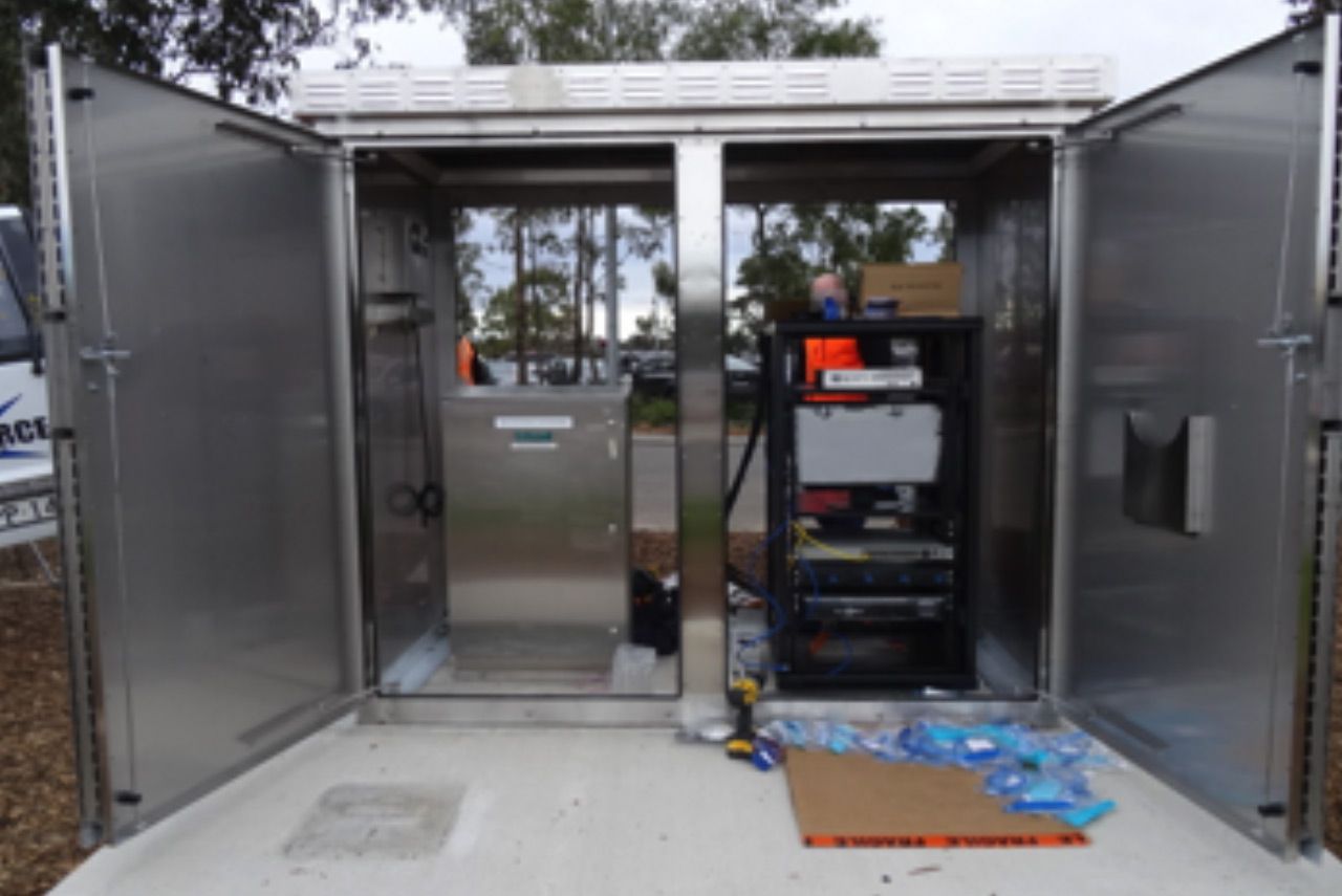 Open utility cabinet with electrical equipment and scattered tools on the floor outdoors