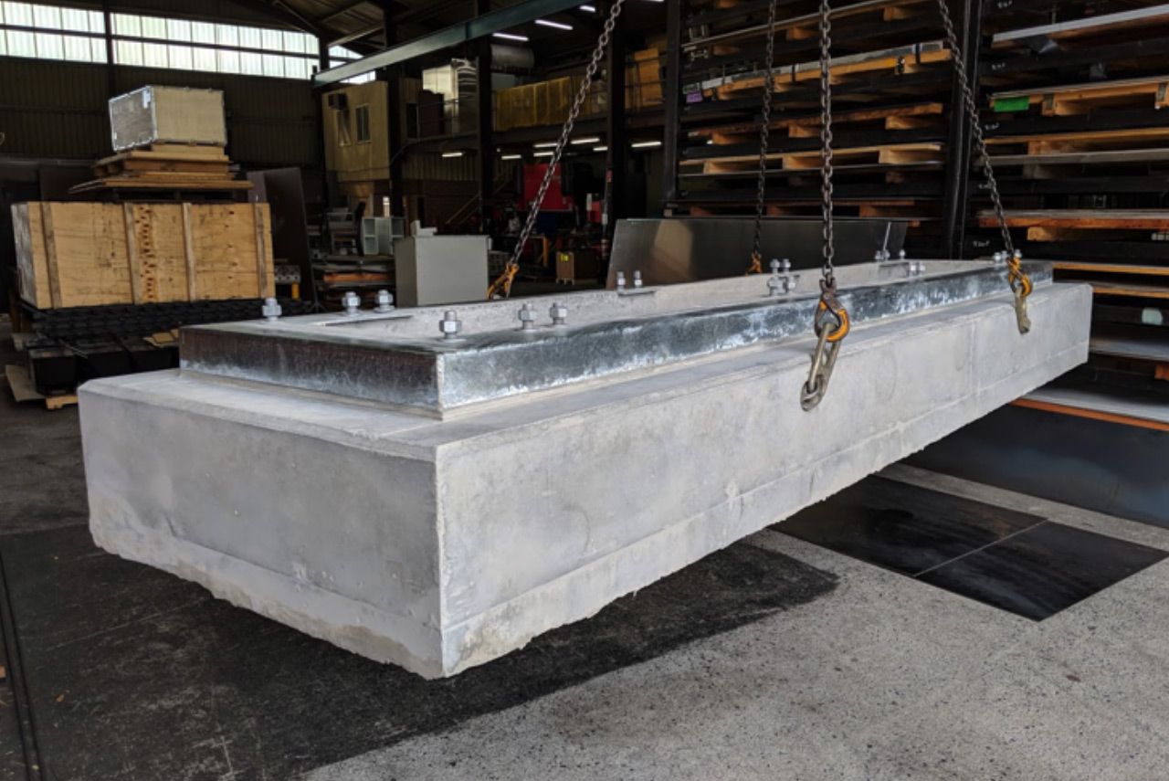 Large concrete industrial mold with metal fittings suspended in a warehouse workshop