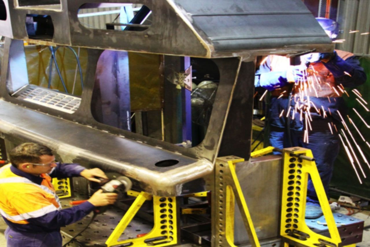 Workers welding a metal frame, with bright sparks in an industrial workshop