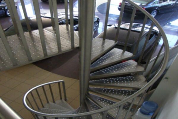 Spiral metal staircase with perforated steps and white railing in a bright indoor space