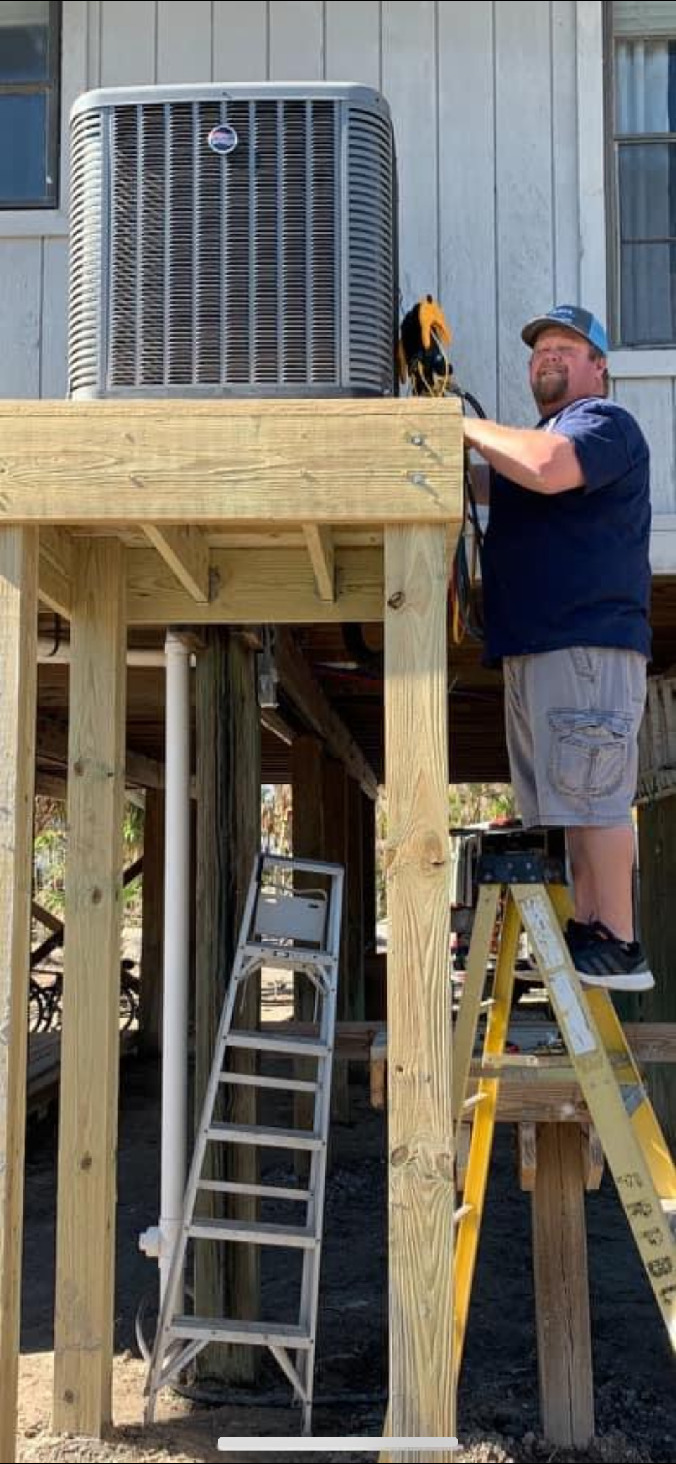 A man is standing on a ladder working on a wooden deck.