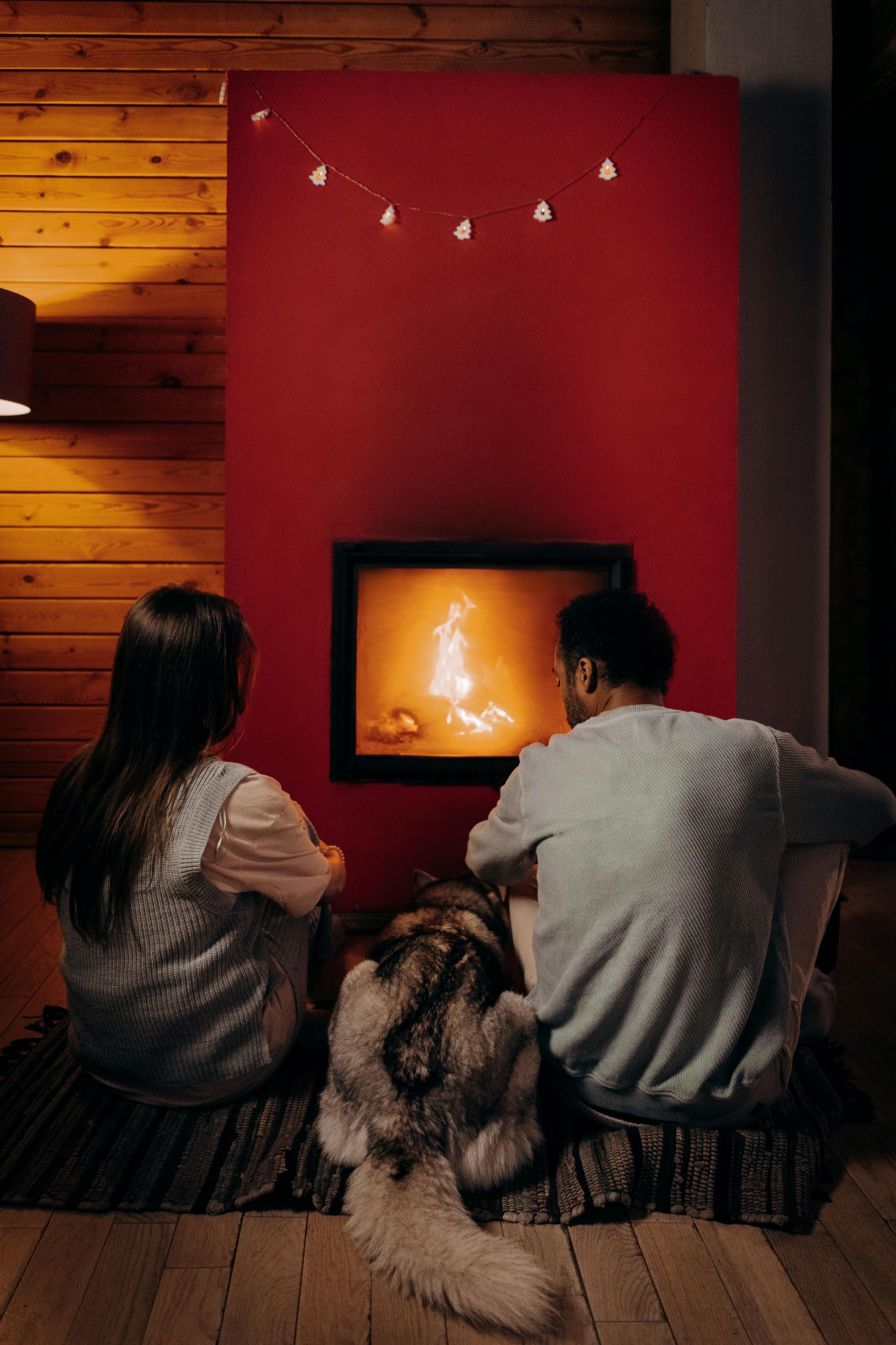 A man and a woman are sitting in front of a fireplace with a dog.