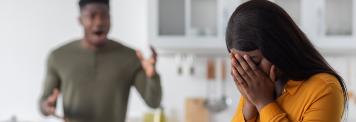 A man is yelling at a woman in a kitchen while she covers her face.