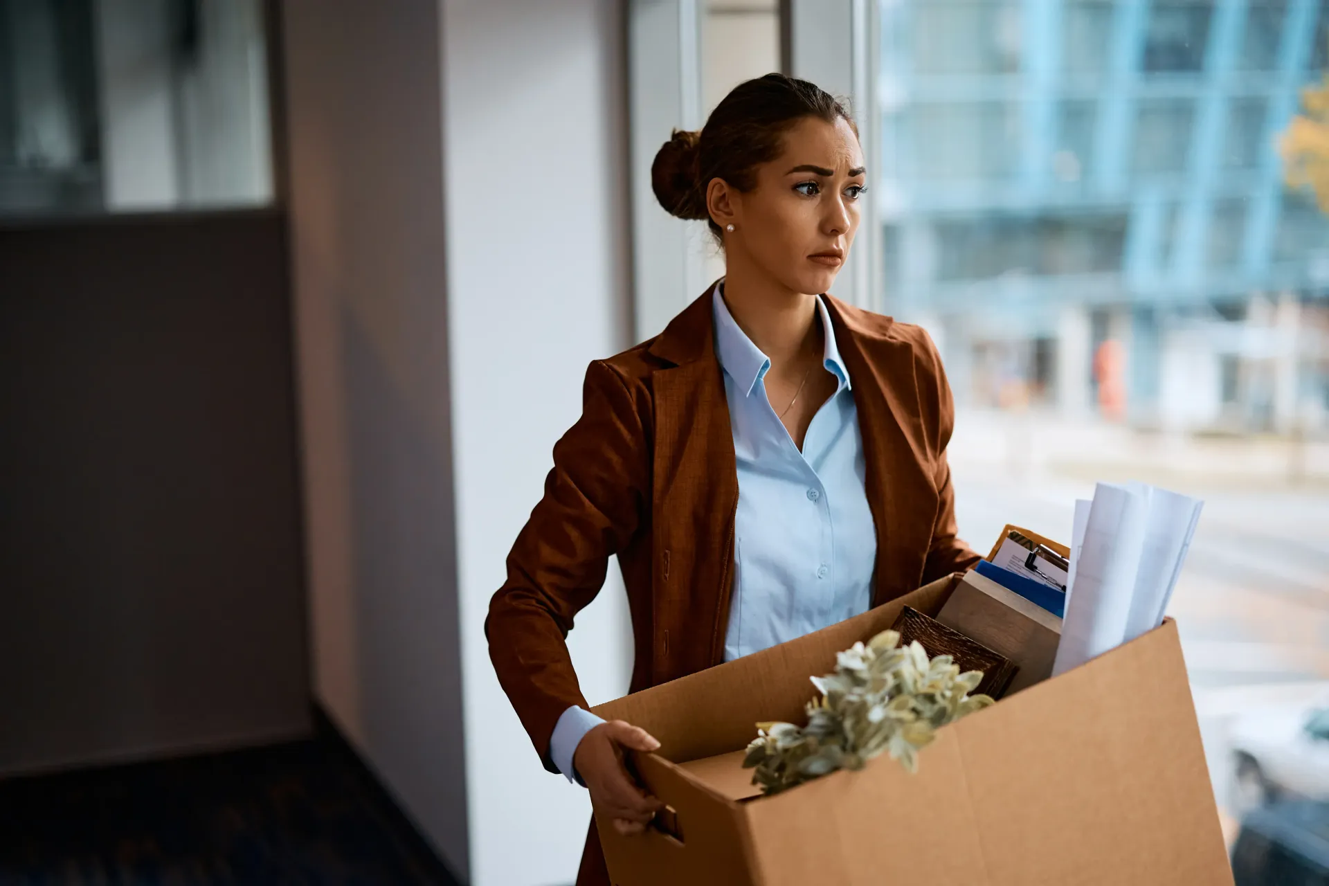 A woman is carrying a box of her belongings out of an office after being fired without warning.