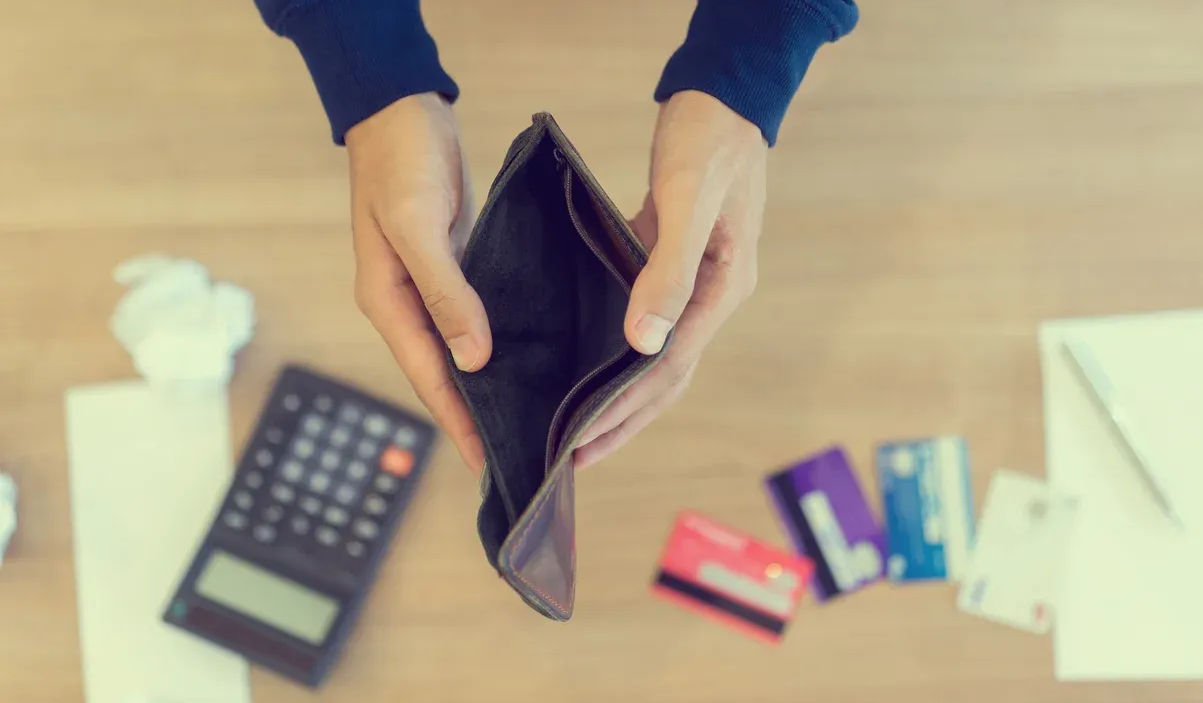 Hands holding an empty wallet, surrounded by credit cards, calculator, and crumpled paper.