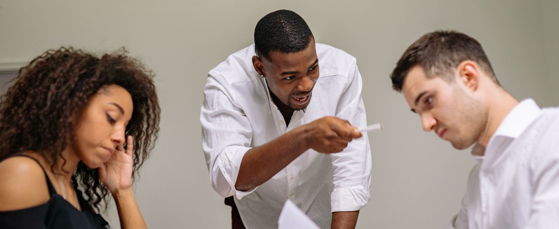 A group of people are sitting around a table and a man is bullying another.