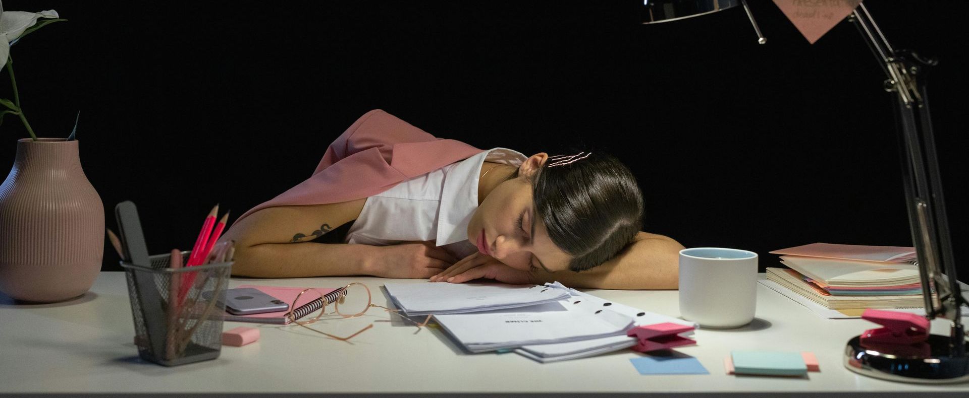 A woman is sleeping at a desk with her head on her work desk, perhaps from overtime working.