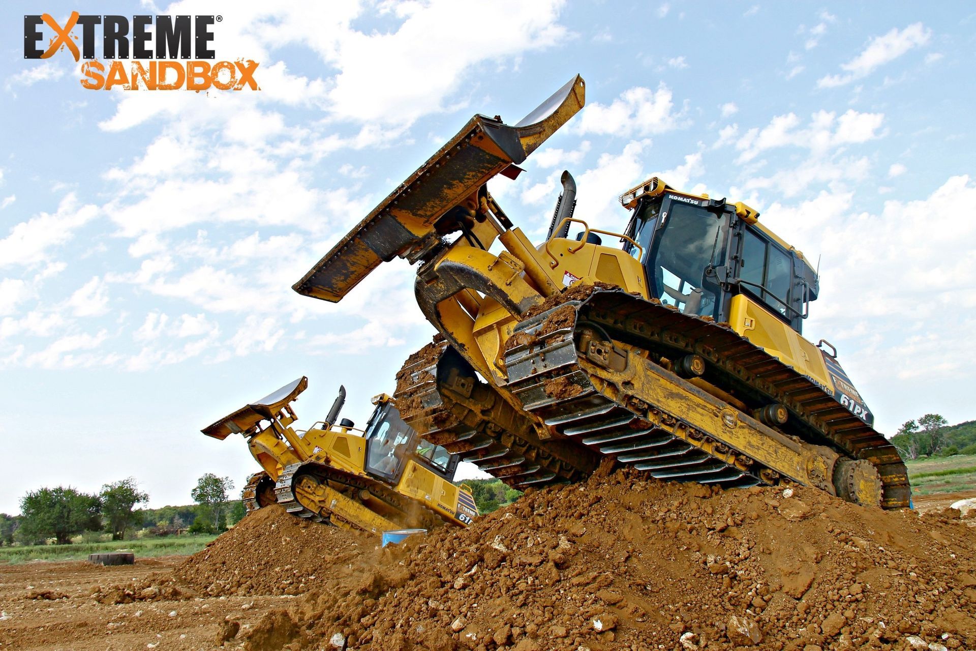 Two yellow bulldozers pushing dirt in a muddy construction site under a blue sky