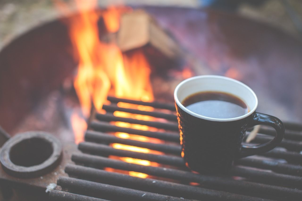 Coffee mug on a grill grate beside a fire pit with flames in the background