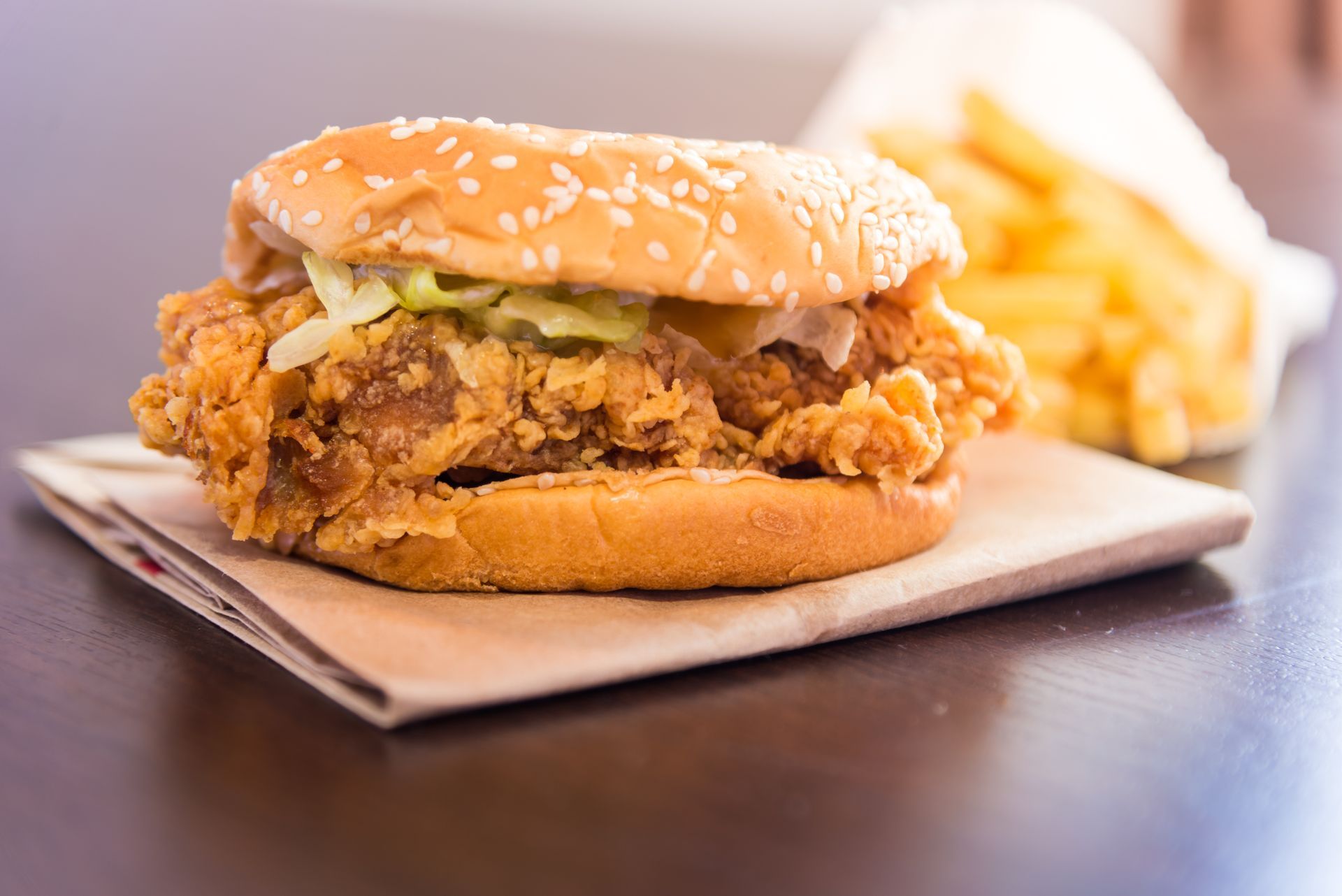 Fried chicken sandwich on a sesame bun with fries in the background