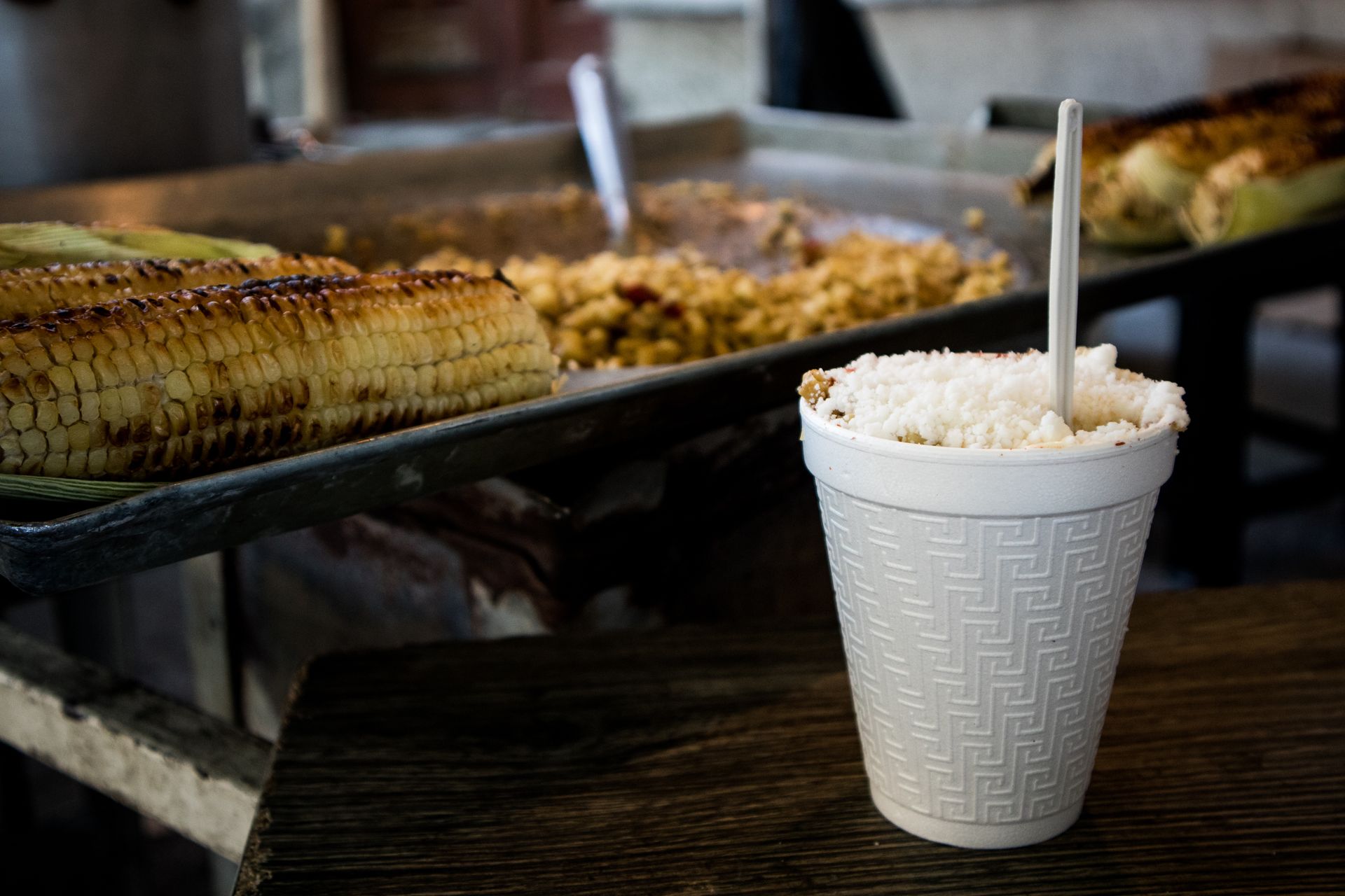 White cup of corn with a spoon beside grilled corn at a street food stall