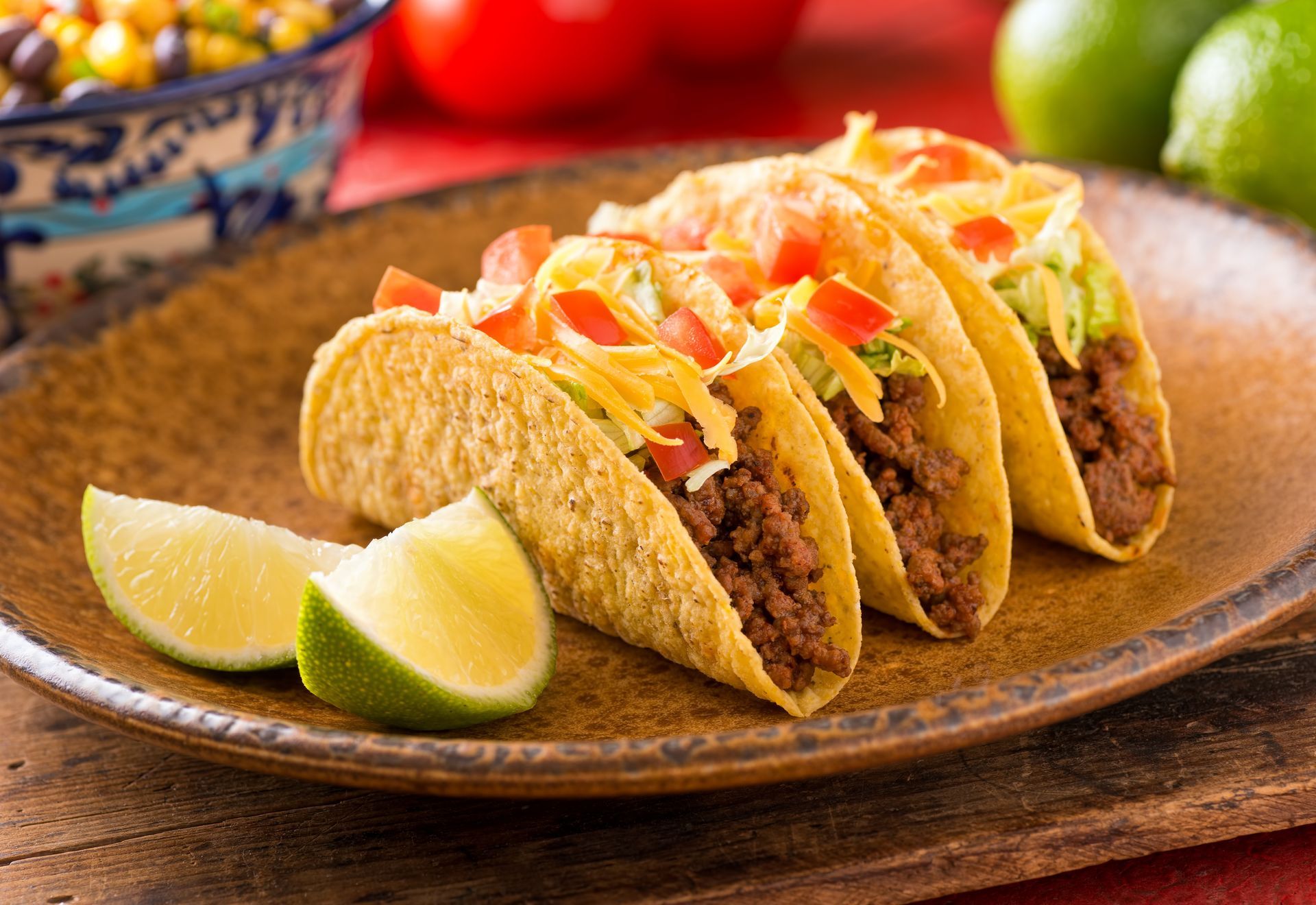 Tacos on a plate with lime wedges and colorful toppings on a wooden table