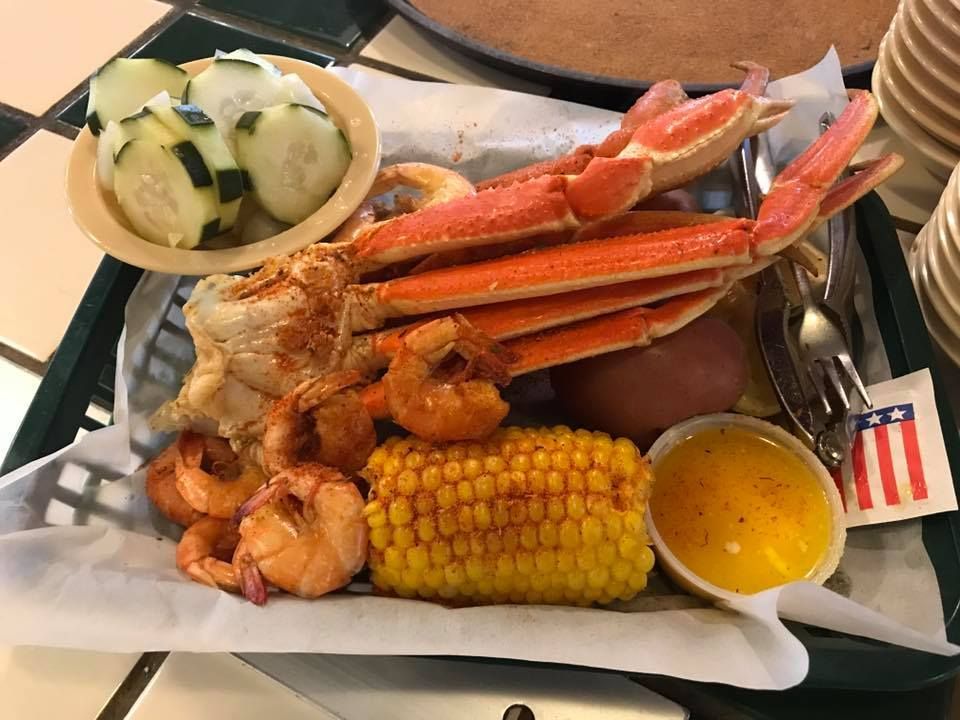 Seafood platter with crab legs, shrimp, corn on the cob, potatoes, and dipping sauces on a tray