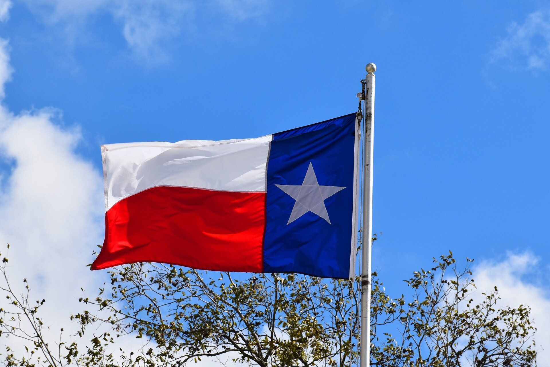 Texas state flag waving against a blue sky with clouds
