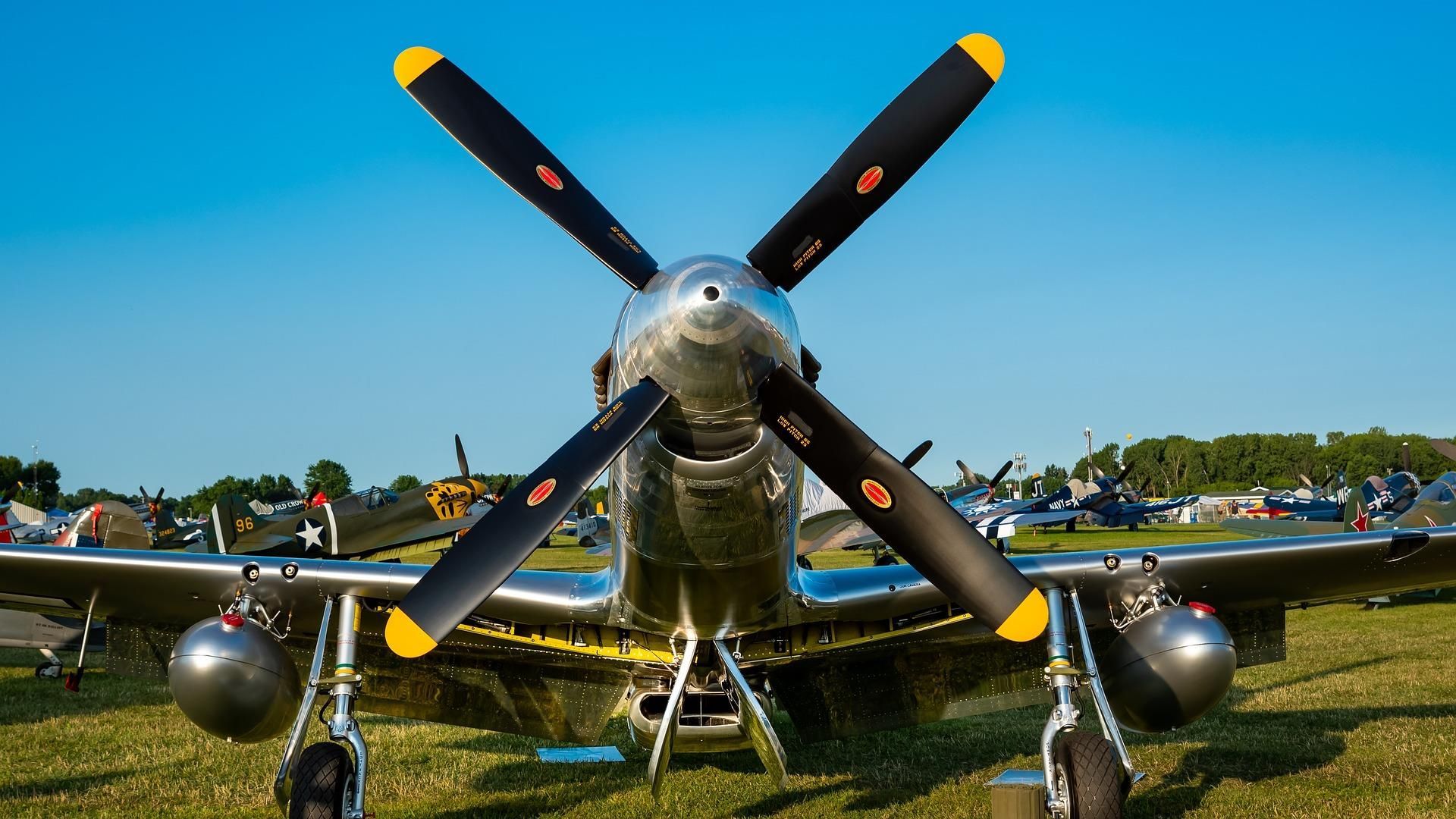 Vintage silver propeller airplane on grassy field under a blue sky, front view