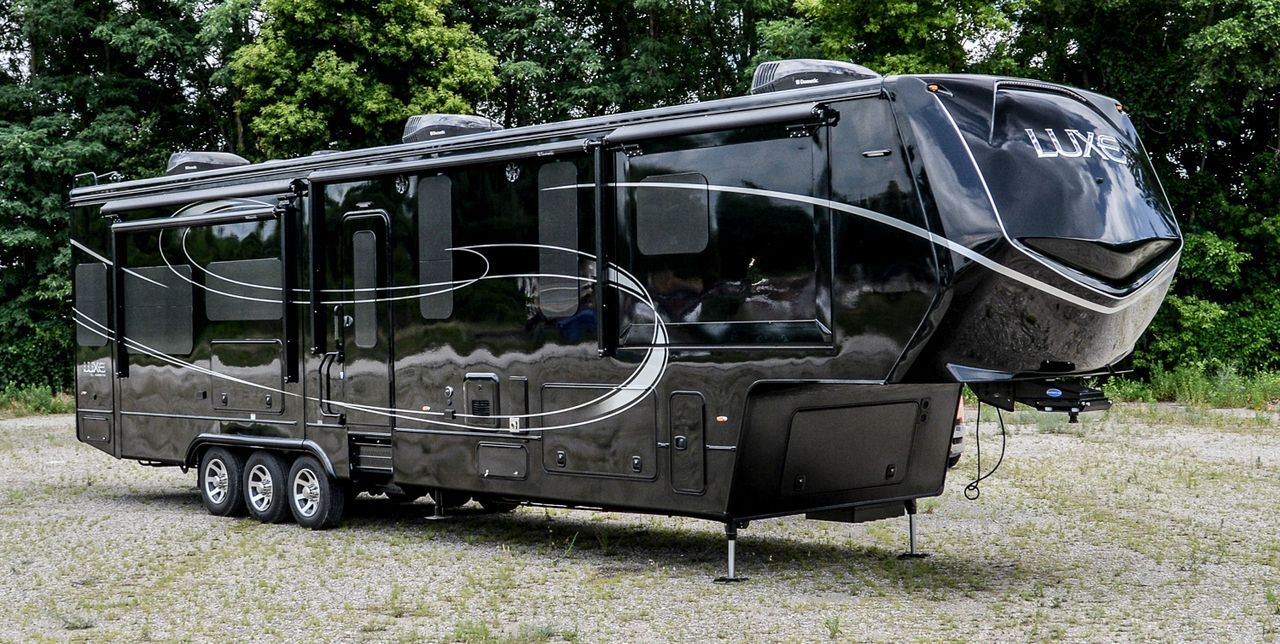 Black luxury RV parked on gravel, with slide-outs extended and front hitch visible.