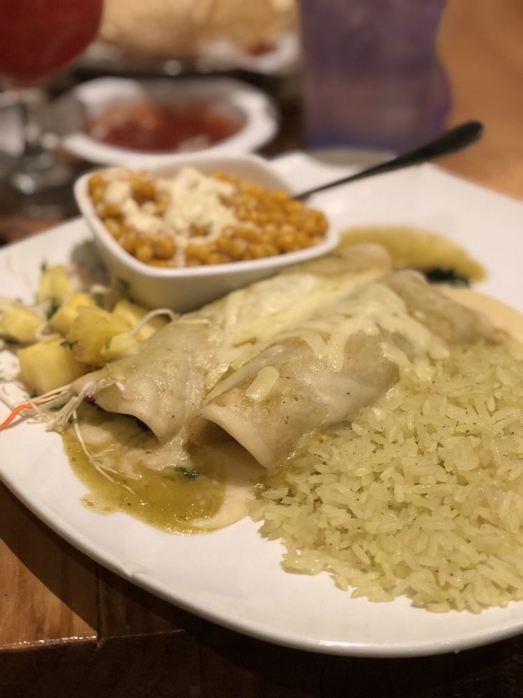 Plate of enchiladas with green sauce and rice, served with beans and a side of salad on a table