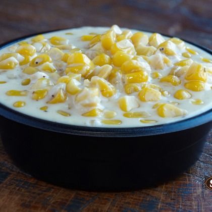 Bowl of creamy corn chowder topped with yellow corn kernels on a wooden surface