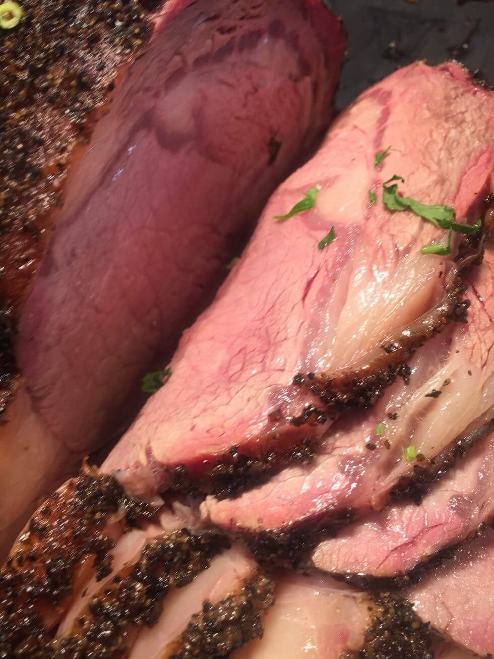 Close-up of sliced pink smoked meat with dark bark and green herb garnish