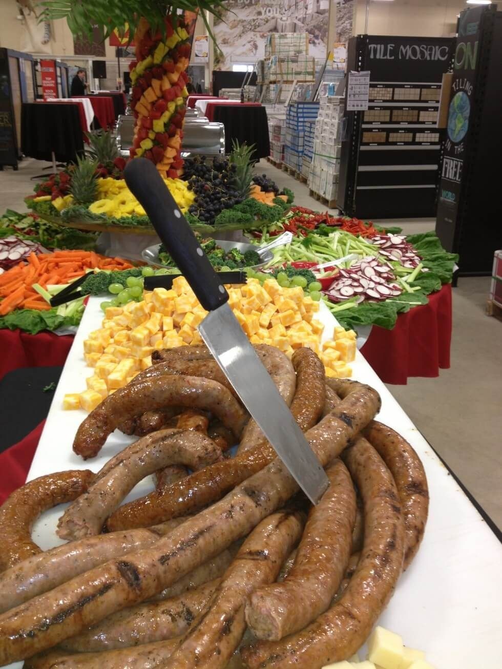 Tray of sausages and yellow potatoes on a buffet table with a knife in the foreground