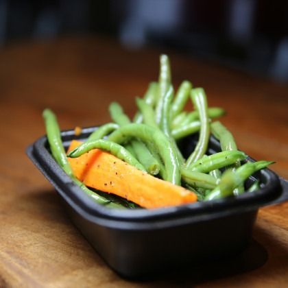Black dish of green beans and a carrot stick on a wooden table
