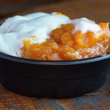 Black bowl of orange dessert topped with whipped cream on a wooden table