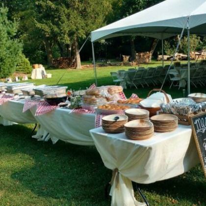 Outdoor buffet setup with tables of food under a white canopy on a grassy lawn