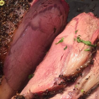 Close-up of raw meat slabs on a grill or smoker, with pink and dark marbled surfaces and herb garnish